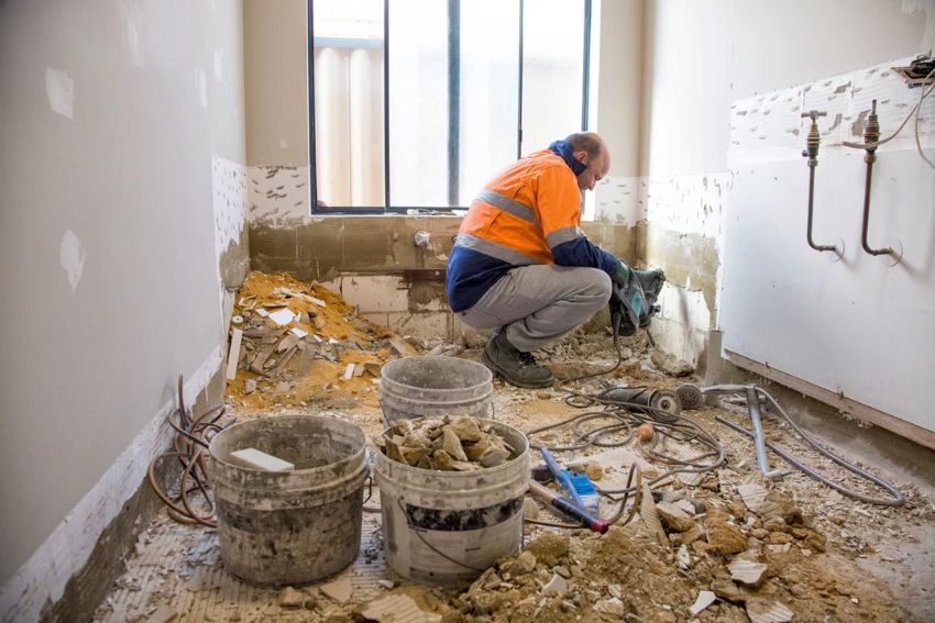 A man in an orange shirt and vest is fixing a bathroom as part of a water damage restoration project in Fort Worth, TX.