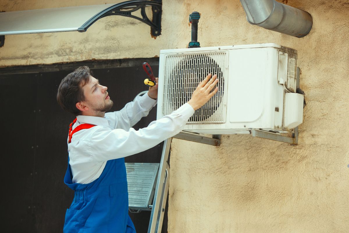 A man in overalls performs maintenance on an air conditioner, emphasizing the importance of regular HVAC upkeep.