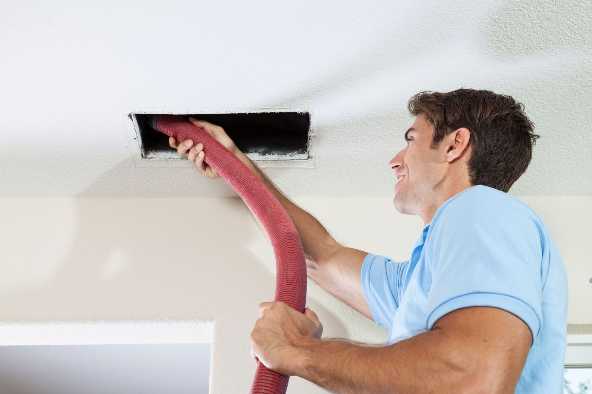 A man using a vacuum hose to clean a ceiling, focusing on air duct cleaning for improved indoor air quality.