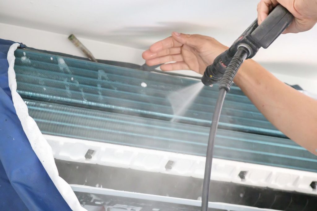 A person cleaning a window air conditioner with a water hose, demonstrating air duct cleaning techniques.